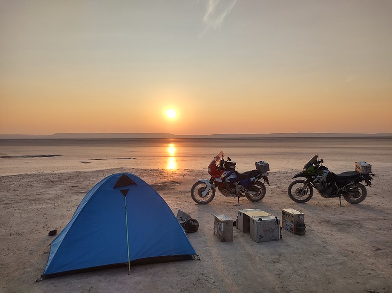 The sun rises over the
          Alford desert behind two motorcycles, panniers as tables and
          chairs and a tent.