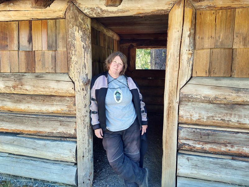 Jayne wearing her Coyotebroad
          shirt as she stands in a recreated CCC cabin doorway.