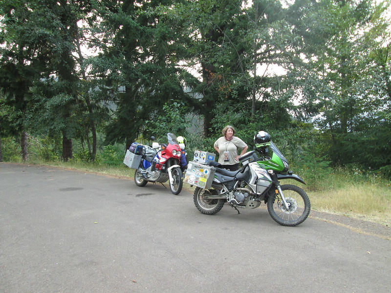 two motorcycles on the side of
          the road. A woman stands behind them looking at the camera.